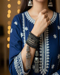 Person wearing a blue embroidered outfit with silver jewelry, including bangles and earrings.
